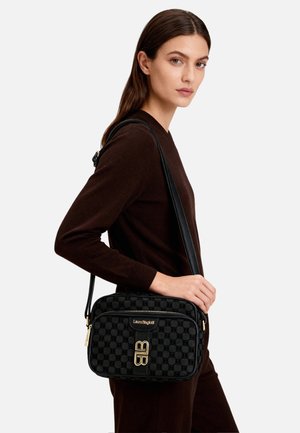 Borsa a tracolla nera con motivo, realizzata in materiale testurizzato, caratterizzata da finiture dorate e chiusura con zip, presentata di lato su un modello.