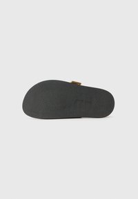 Semelle d'une sandale gris clair, en matériau en caoutchouc texturé. Présente un design minimaliste avec un accent en métal doré.