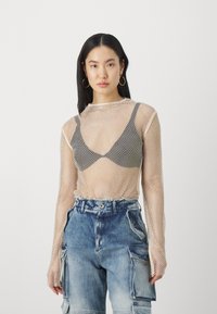 Mesh langermet topp i lys beige, lagd over en svart bh. Kombinert med blå denim cargo bukser med flere lommer og en avslappet passform.