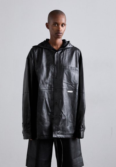 Veste surdimensionnée en cuir noir avec capuche, dotée d'une fermeture à boutons, d'une poche poitrine et d'un logo de marque discret. Fini lisse et texturé.