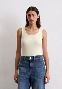 Lys gul ribbet tanktop med rund hals, sammen med høyt liv blå denimjeans med doble frontlommer og knappelukking.