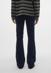 Pull rayé gris et noir, associé à un pantalon en velours côtelé évasé bleu marine, vu de dos. Le pull a une coupe décontractée et une texture côtelée.