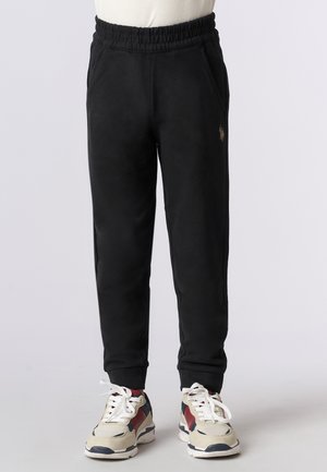 Pantaloni della tuta neri realizzati in materiale morbido, dotati di una cintura elastica, tasche laterali e un piccolo dettaglio con logo. Abbinati a sneakers multicolori.