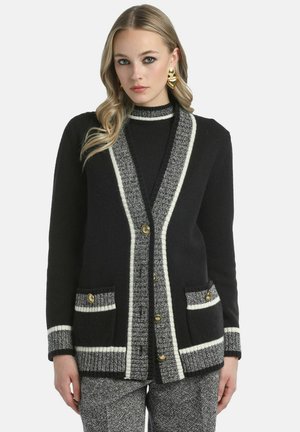 Zwarte cardigan met een gestructureerde, patroon voorzijde, witte details langs de randen en twee voorzakken. Gouden knopelementen zichtbaar.