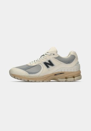 Baskets New Balance beige et gris avec des panneaux en maille et en daim, logo "N" sur le côté, semelle rembourrée, et "2002" imprimé près du talon.
