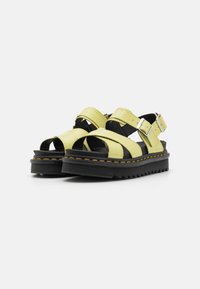 Sandalias de cuero amarillo con amplias correas entrecruzadas, hebillas ajustables, suelas de goma negra y costuras amarillas en contraste.