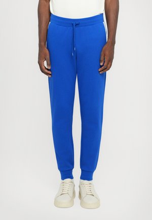 Blå sweatpants lavet af blødt stof med elastisk talje og sidelommer; tapered ben design og ribbede manchetter. Sammen med lette sneakers.