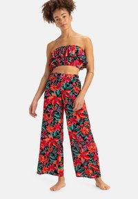 Blumiges Zweiteiler-Outfit: Rüschentop ohne Träger mit lebhaften roten und grünen Blumenmustern, kombiniert mit weitem Hosenbein mit ähnlichem Design.
