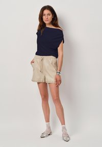 Marine off-shoulder top, beige drawstring shorts met metallic studs, zilveren platte schoenen en kant sokken. Eenvoudige, relaxte pasvorm.