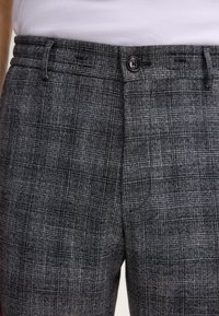 Pantalons à carreaux gris avec une coupe ajustée, dotés d'une fermeture à bouton, de passants de ceinture et d'un motif de tissu texturé.