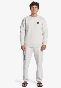 Felpa crewneck e pantaloni sportivi in felpa grigia chiara. Presenta una toppa con logo e stampa laterale del logo. Texture morbida con polsini e orlo a costine.