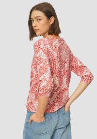 Geprinte blouse in tinten van roze met driekwartmouwen. Beschikt over een ronde halslijn en een textuurstof met een bloemmotief.