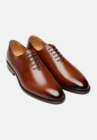 Chaussures en cuir marron à lacets avec une finition lisse, un bout pointu, des coutures minimales et un design élégant. Présente des accents marron foncé sur la semelle.