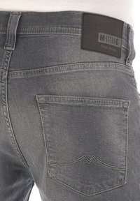 Jeans de mezclilla gris con bolsillos traseros de diseño puntiagudo y una etiqueta de cuero negra en la cintura, grabada con "MUSTANG True Denim."