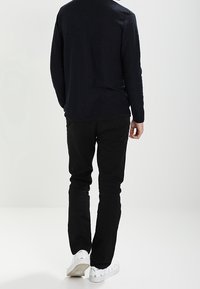Dlouhý rukáv, tmavý pletený svetr v kombinaci s černými kalhotami a bílými teniskami. Oblečení má uvolněný střih a minimalistický design.