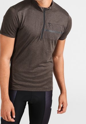 T-shirt de sport gris foncé à manches courtes avec fermeture éclair à l'avant et poche poitrine zippée, porté par une personne portant un short de cyclisme noir.