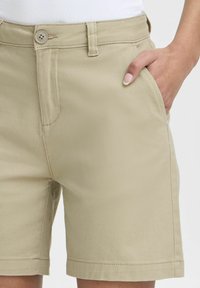 Pantaloni shorts khaki realizzati in tessuto leggero con una finitura liscia, dotati di chiusura frontale con bottone e tasche laterali.