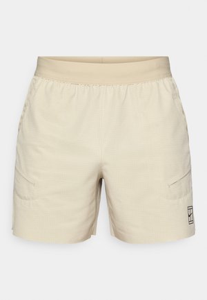 Pantaloncini beige chiaro con motivo intrecciato, vita elastica, tasche laterali e un logo sottile sulla parte inferiore della gamba destra. Tessuto dalla texture liscia.