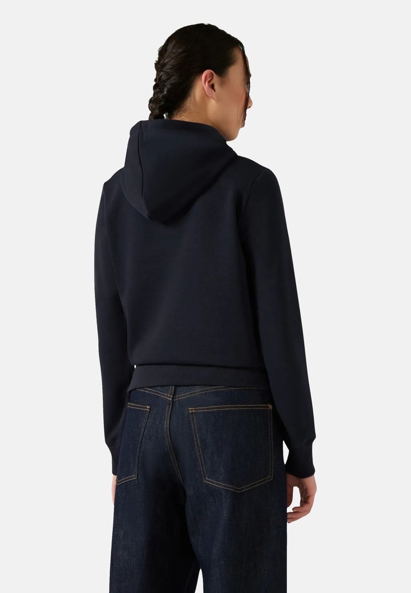 Felpa navy con tasca a canguro, orlo a costine e cappuccio regolabile con cordino, abbinata a jeans in denim scuro con tasche posteriori cucite.