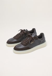 Dark brown leather and suede sneakers with perforated design, brown laces, and a cream rubber sole. Gold branding on the side.