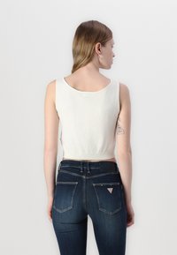 White cropped tank top with a rounded neckline, ribbed hem, and smooth texture, paired with dark blue, form-fitting jeans featuring back pockets.