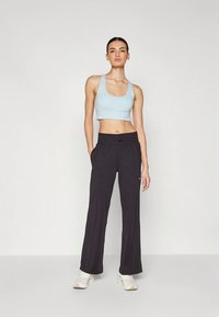 Világoskék sportmelltartó és bő, fekete nadrág. A nadrágon húzózsinóros derékrész és finom logórészlet található. Az összeállítást sportcipő egészíti ki.