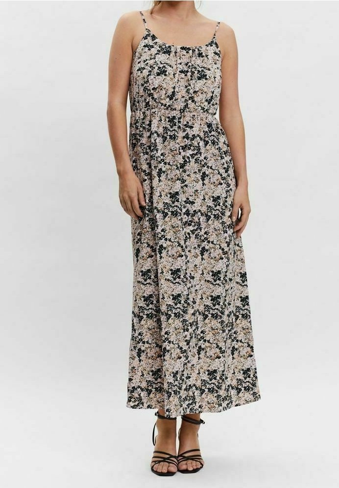 Femme portant une robe maxi fleurie sans manches avec de fines bretelles et des sandales noires à lanières, debout devant un fond uni.