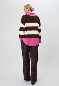 Ruskea ja kerma raidallinen villapaita, jossa on vaaleanpunainen kaulus ja helma, yhdistettynä leveälahkeisiin leopardikuvioisiin housuihin. Pehmeä neulosmateriaali, rento malli.