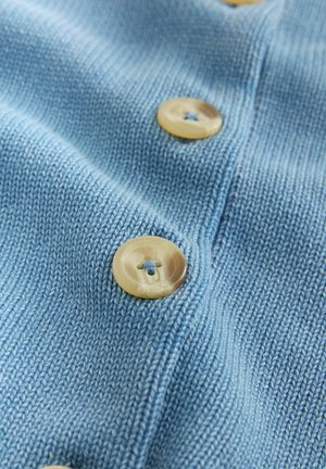Un tissu tricoté bleu clair comportant deux boutons en matière beige, avec une texture subtile.