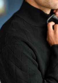 Czarny sweter z dzianiny z wysokim kołnierzem, z teksturowanym wzorem w diamenty. Zamek błyskawiczny i ściągacze u rękawów podkreślają jego design.