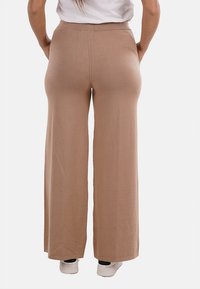 Pantaloni a gamba larga in morbido tessuto beige, con vita alta, texture liscia e fit rilassato; abbinati a sneakers bianche.