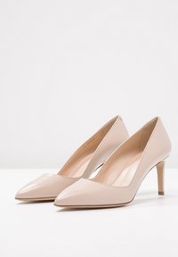 Escarpins en cuir verni beige avec un bout pointu et un talon fin, présentant une surface lisse et un design minimaliste.