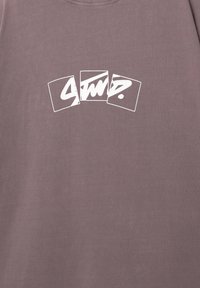 Grå-lilla bomulds T-shirt med et hvidt grafisk design af overlappende rektangulære former med stiliseret tekst i midten.