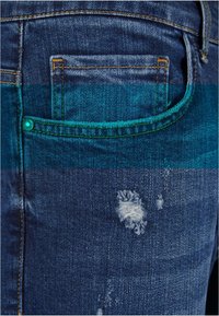 Vaqueros de mezclilla azul oscuro con un pequeño bolsillo trasero, costuras naranjas y detalles deshilachados en la tela. Texturizados con un aspecto desgastado.