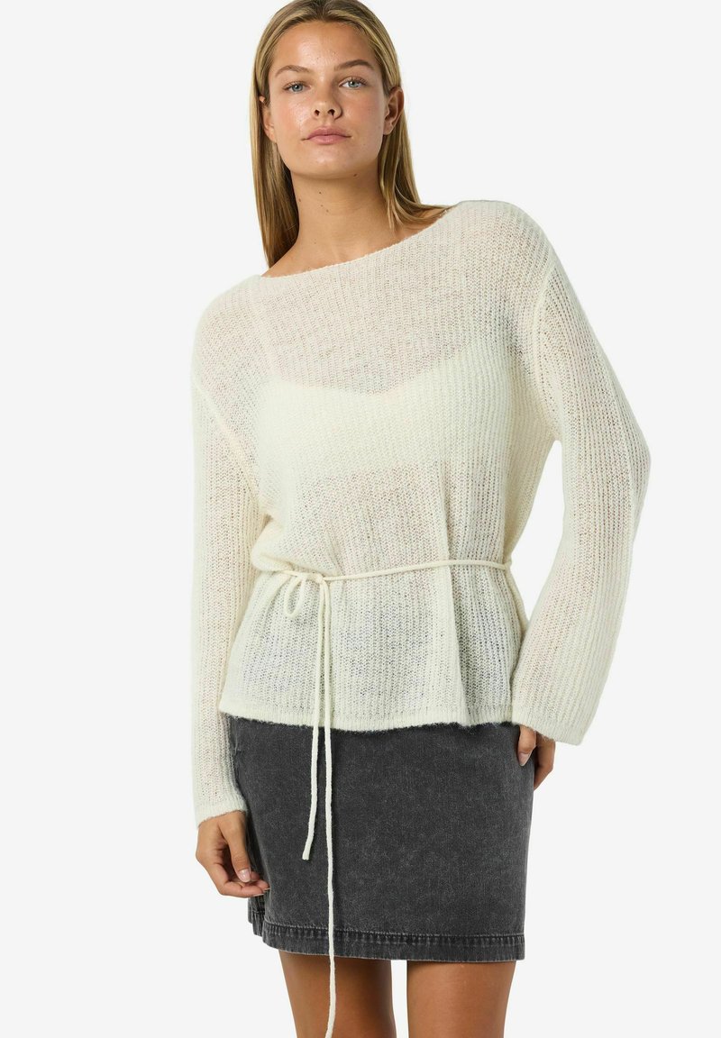 Maglione crema a maglia con vestibilità comoda e cintura annodata in vita, abbinato a una gonna di denim grigio scuro. Presenta maniche lunghe e una texture morbida.
