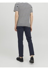 Randig crew neck t-shirt i off-white och marinblå, i kombination med marinblå byxor. Svarta skor med uppvikta benslutar. Minimalistisk design, avslappnad passform.