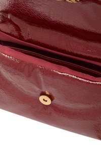 Burgundská lakovaná kůže taška s texturovaným povrchem, obsahující zlaté magnetické zapínání a měkkou textilní podšívku s vnitřní kapsou.