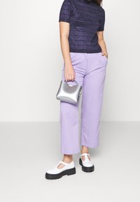 Purppuranväriset leveälahkeiset housut, laivastonsinisestä teksturoidusta lyhythihaisesta paidasta ja valkoiset T-nauhakengät mustilla paksuilla pohjilla, kädessä hopeinen clutch-laukku.