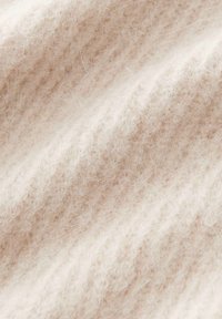 Tissu doux et moelleux de couleur crème avec une texture côtelée en tricot, en gros plan.