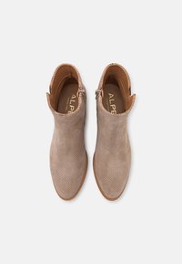 Vaaleanbeige rei'itetyt nilkkurit, joissa on sileä nahkavuori, sivuvetoketjut ja teksturoitu pohja. Ominaisuuksiin kuuluu mantelinmuotoinen varvas.