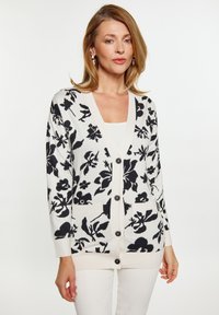 Cardigan leggero con una base crema e un motivo floreale nero, chiusura con bottoni e due tasche frontali. Maniche lunghe con polsini a costine.
