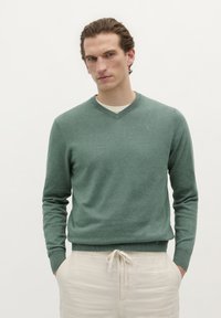 Groene v-hals trui van een zachte gebreide stof, met lange mouwen en geribde manchetten, gecombineerd met lichtgekleurde broek met aantrekkoord.