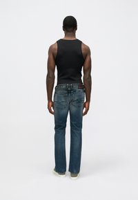 Camisola preta sem mangas, jeans azuis de perna reta com desbotamento, detalhes em pele e logotipo na parte de trás. Usada com ténis brancos.