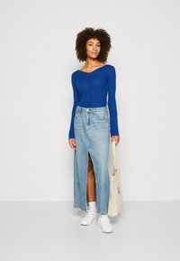 Blå langermet topp med ribbet tekstur, kombinert med en lyseblå denimmaxiskjørt med splitt foran, og hvite sneakers.