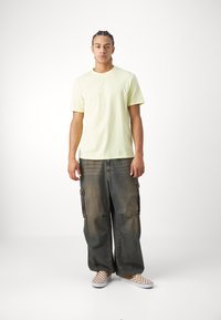 Svetložlté tričko s okrúhlym výstrihom, voľné tmavo-denim cargo nohavice s bočnými vreckami a kockované slip-on topánky. Minimalistický dizajn a ležérny štýl.