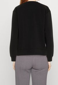 Svart sweatshirt med långa ärmar, rundad hals och ribbade muddare; har en slät textur och en avslappnad passform.