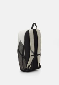Sac à dos gris et noir au design épuré, avec des poches latérales en mesh, des bretelles réglables et une poignée supérieure pour un transport facile.