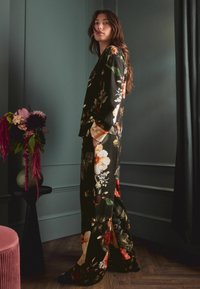 Mustaline lillemusteridega musta värvi vabaaja komplekt, mis koosneb pika varrukaga topsist ja laiade jalgadega pükstest, valmistatud pehmest, tekstuuriga kangast.