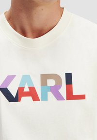 Cream-colored sweatshirt featuring large multicolored block letters spelling "KARL" in red, blue, purple, teal, and beige.