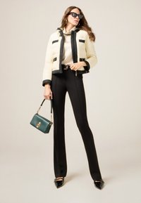 Chaqueta acolchada en crema y negro, pantalones negros de cintura alta y un bolso verde; la modelo lleva gafas de sol y zapatos negros puntiagudos.